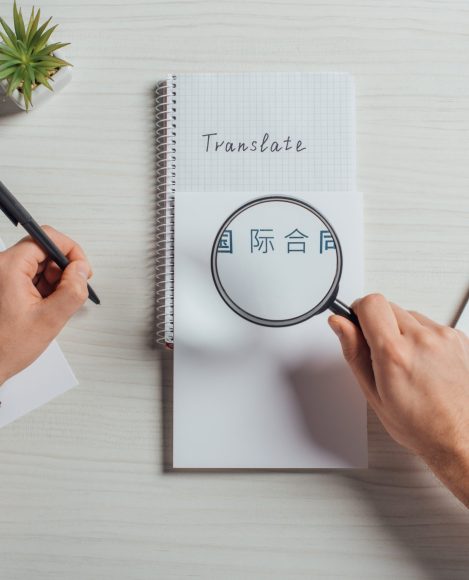 cropped view of translator working with hieroglyphics, laptop and magnifying glass